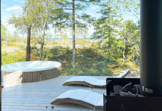 Vue depuis le chalet à VÄDDÖ, Suède, avec jacuzzi extérieur, chaises longues et forêt verdoyante.