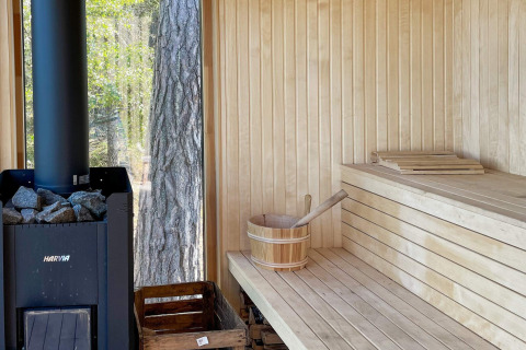 Moderne sauna met houten interieur, Harvia-kachel en uitzicht op bos in vakantiehuis in VÄDDÖ, Zweden.