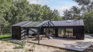Maison de vacances cinq étoiles à Læsø, grande terrasse en bois et verrière, entourée de forêt.