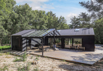 Maison de vacances cinq étoiles à Læsø, grande terrasse en bois et verrière, entourée de forêt.