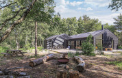 Modernes schwarzes Ferienhaus auf Læsø, Dänemark, mit Holzsitzplätzen und Feuerstelle im Grünen.