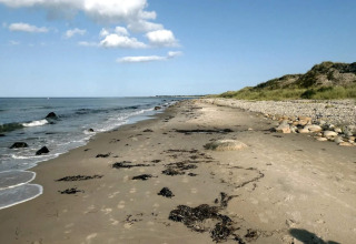 Rustig zandstrand met stenen op Læsø, Denemarken, naast 5-sterren vakantiehuis bij een heldere blauwe lucht.