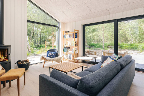 Moderne stue i et femstjernet feriehus i Læsø, Danmark, med store vinduer og naturskøn udsigt.