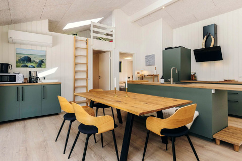 Cuisine moderne et salle à manger avec table en bois, armoires vertes et échelle, dans un lodge à Læsø, Danemark.