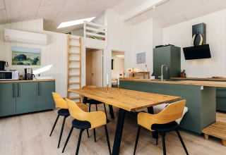 Cuisine moderne et salle à manger avec table en bois, armoires vertes et échelle, dans un lodge à Læsø, Danemark.