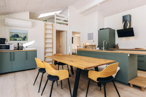 Cucina moderna e zona pranzo con tavolo in legno, mobili verdi e scala in una casa a Læsø, Danimarca.