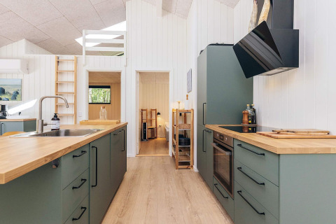 Cocina moderna con gabinetes verdes y encimeras de madera en una casa de vacaciones de 5 estrellas en Læsø, Dinamarca.