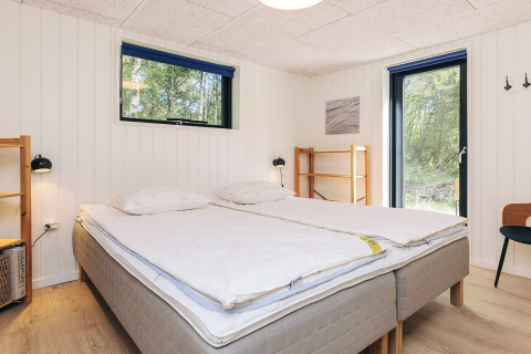 Soveværelse med dobbeltseng, lyse trævægge og store vinduer på 5-stjernet feriehus i Læsø, Danmark.