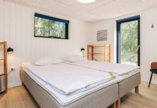 Bedroom with double bed, wood shelves and large windows at 5 star holiday home in Læsø, Denmark.