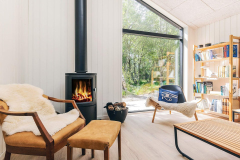 Lys stue i et sommerhus på Læsø, Danmark, med pejs, lænestole og udsigt til natur gennem vinduet.