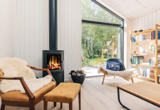 Bright living room in a holiday lodge in Læsø, Denmark, with fireplace, cozy chairs, and forest view.