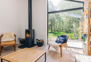 Moderne stue i feriebolig på Læsø med brændeovn, store vinduer, komfortable stole og udsigt til natur.