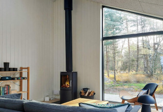 Salón moderno y luminoso en casa vacacional 5 estrellas en Læsø, Dinamarca, con estufa y gran ventanal.