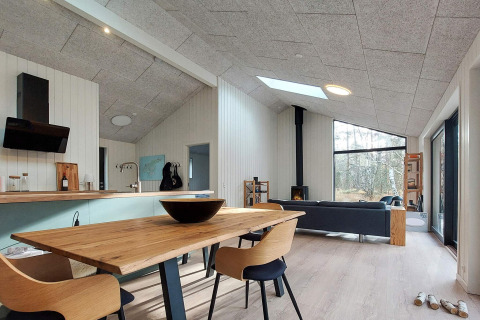 Intérieur moderne d'une maison de vacances à Læsø, Danemark, avec table à manger, poêle et vue forêt.