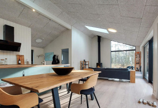 Moderne interiør i feriehus på Læsø, med spisebord, brændeovn og store vinduer til skoven udenfor.