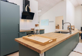 Moderne keuken in vijfsterren vakantiehuis in Læsø, Denemarken, met houten blad en groene kasten.