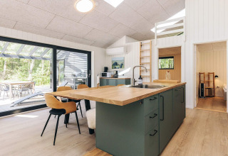 Modern kitchen and dining area in a holiday home in Læsø, Denmark, with view of terrace and nature.