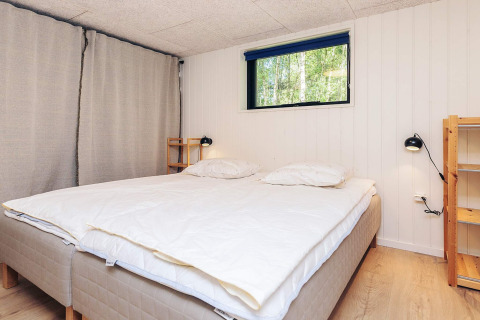 Dormitorio en una casa vacacional de 5 estrellas en Læsø, Dinamarca, con cama doble y estantes de madera.