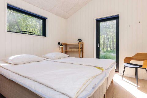 Bright bedroom in a holiday lodge on Læsø, Denmark, featuring a double bed, wood walls, and nature views.