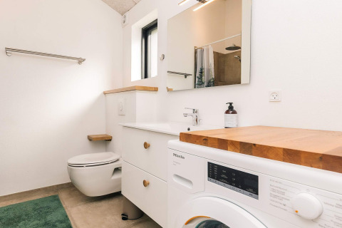 Moderne badkamer met wasmachine, hout aanrecht, hangtoilet en grote spiegel in de Læsø lodge.