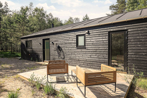 Maison de vacances noire moderne à Læsø, Danemark, avec terrasse en bois et mobilier extérieur en forêt