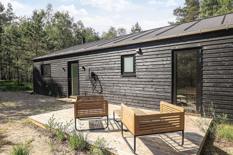 Sort træferiebolig med moderne havemøbler på træterrasse, omgivet af grønne træer i Læsø, Danmark