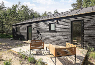 Modern black wooden holiday lodge in Læsø, Denmark, with outdoor seating and surrounded by green forest