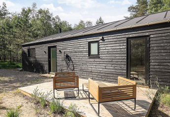 Modern zwart houten vakantiehuis met terras en tuinmeubilair in Læsø, Denemarken, omringd door groen