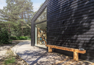 Udendørs træterrasse og bænk ved et moderne sort sommerhus med stor vinduesfacade i Læsø, Danmark.