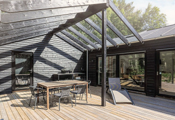 Terrasse avec mobilier moderne et toit partiel en verre d'une maison de vacances 5 étoiles à Læsø, Danemark