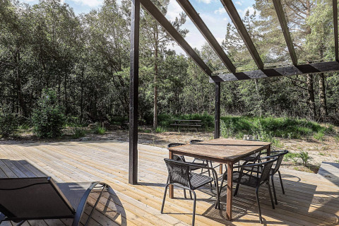Holzterrasse mit Esstisch und Stühlen unter einer Pergola, Ferienhaus in Læsø, umgeben von Wald.