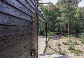 Udendørs bruser monteret på sort trævæg ved feriebolig i Læsø, Danmark, omgivet af natur og terrasse.