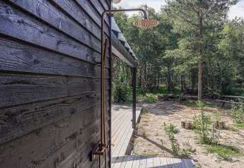 Buitendouche aan een zwarte houten wand van een vakantiehuis op Læsø, Denemarken, met uitzicht op het bos.
