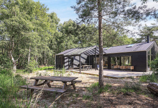 Modern vijfsterren vakantiehuis op Læsø, Denemarken, met houten terras en picknicktafel in het bos.