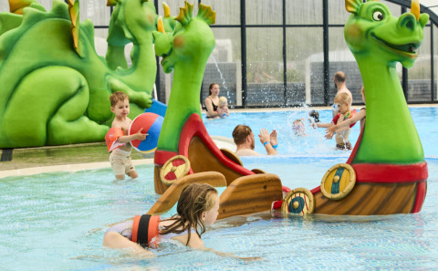 Kinder spielen im Schwimmbad mit grünen Drachenfiguren und Booten im Horsens City Camp in Dänemark.