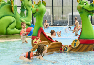 Kinder spielen im Schwimmbad mit grünen Drachenfiguren und Booten im Horsens City Camp in Dänemark.