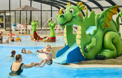 Children play in an indoor pool with a green dragon waterslide at Horsens City Camp holiday park, Denmark.