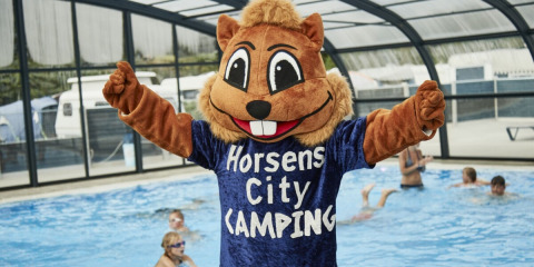Mascotte en costume d’écureuil devant piscine couverte avec enfants à Horsens City Camping au Danemark.