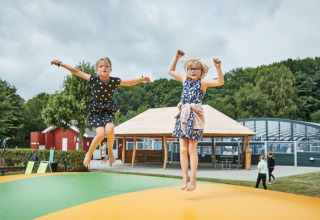 Zwei Kinder springen auf einem Hüpfkissen im Horsens City Camp in Dänemark, umgeben von Natur und Spielplatz.