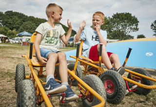 Twee jongens op gocarts geven elkaar een high five in Horsens City Camp, een vakantiepark in Denemarken.