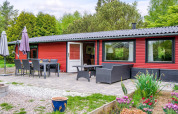 Udendørs terrasse med spisebord og loungemøbler foran en rød feriebolig i grønt område i Holbæk, Danmark.