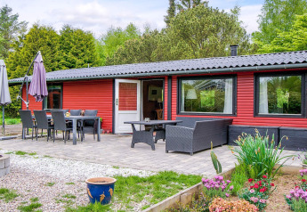Udendørs terrasse med spisebord og loungemøbler foran en rød feriebolig i grønt område i Holbæk, Danmark.