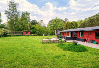 Grand jardin vert avec maison de vacances rouge à Holbæk, Danemark. Terrasse extérieure, parterres et filet de volley.