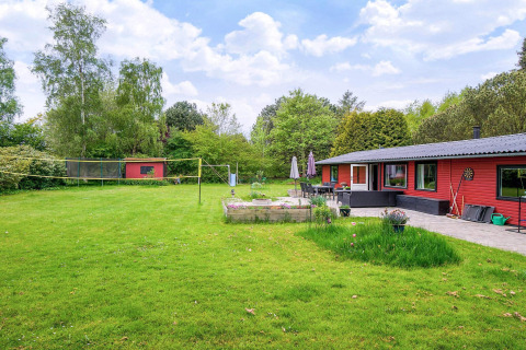 Grote groene tuin met rood vakantiehuis in Holbæk, Denemarken. Terras, bloembakken en volleybalnet.