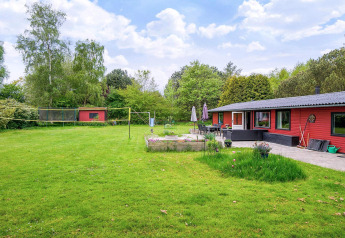 Grand jardin vert avec maison de vacances rouge à Holbæk, Danemark. Terrasse extérieure, parterres et filet de volley.