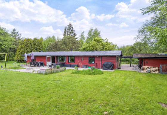 Vue extérieure d'une maison de vacances rouge pour 8 personnes à Holbæk, entourée de pelouse et d'arbres verts.