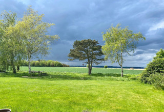Udsigt fra 8 personers feriehus i Holbæk, Danmark, med grønne marker, træer og dramatisk himmel.