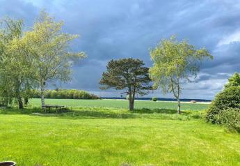 Uitzicht vanaf 8-persoons vakantiehuis in Holbæk, Denemarken, met groene velden, bomen en bewolkte lucht.