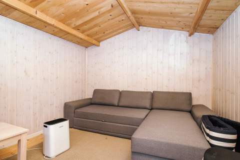 Soggiorno accogliente con divano grigio ad angolo, soffitto in legno e depuratore d’aria moderno.