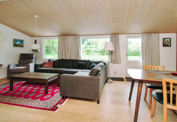 Woonkamer met hoekbank, eettafel, rood vloerkleed en grote ramen in 8 persoons vakantiehuis in Holbæk, Denemarken.